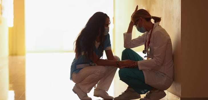 A female doctor calms down a tired colleague in the clinic, close-up. Stress of medical staff during a pandemic