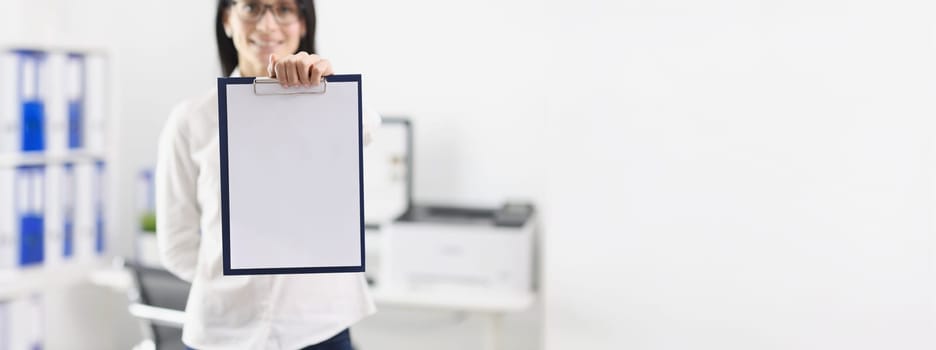 Woman in the office shows a folder with a blank document, mock up, close-up, blurry. Workspace, mentor businesswoman