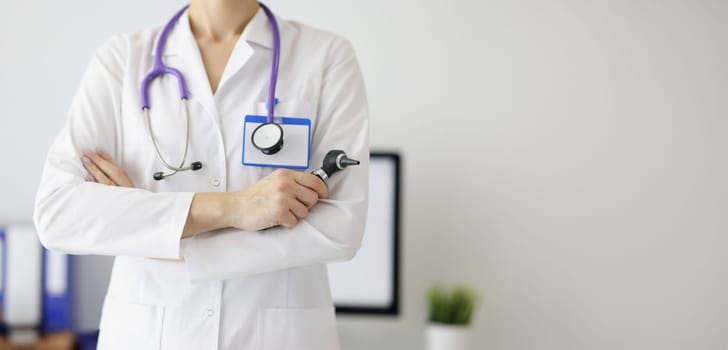 A woman otolaryngologist in a white coat holds an otoscope, close-up. Laryngologist consultation, clinic visit