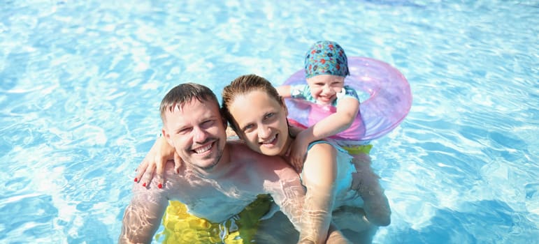 Husband with wife and child swim together in the pool, close-up. Happy family having fun in blue transparent water