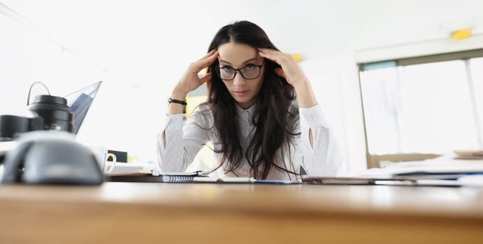 Young woman sits at the table in stress at work. Fatigue of office staff, emotional burnout, career problems