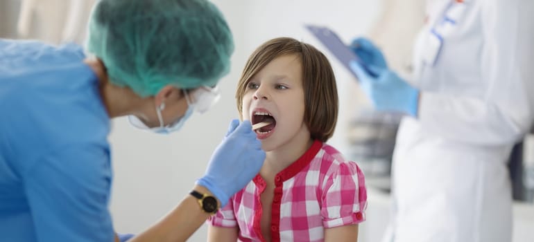 The doctor in the clinic looks at the throat of a little girl, close-up, blurry. Examination of a child by a pediatrician, diagnostics