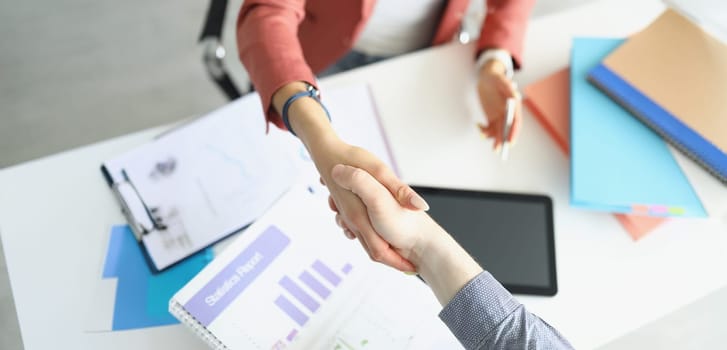 A woman in the office shakes hands with a man, there is a statistical report on the table, close-up, blurry. Approval of the report