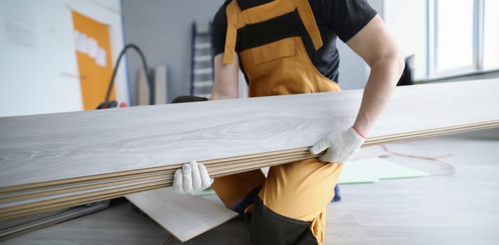 A man in uniform holds laminate panels, close-up. Repair in the apartment, replacing the floor covering in the room, laying parquet