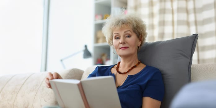 An elderly woman reads a book at home, close-up, blurry. Retirement age, leisure time during a pandemic