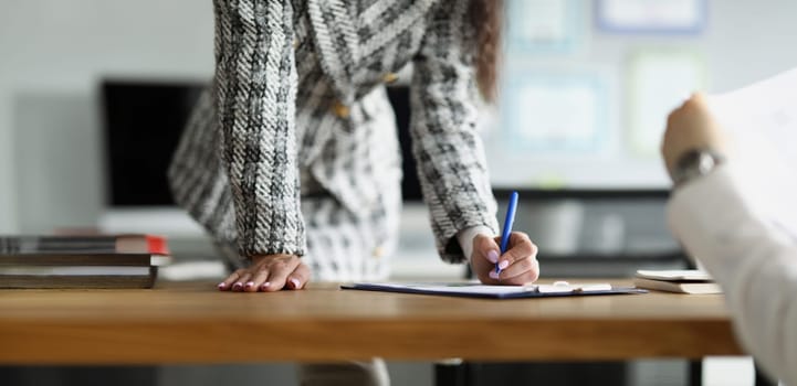 A woman in the office in the presence of a man signs documents, close-up, blurry. Dismissal of an employee