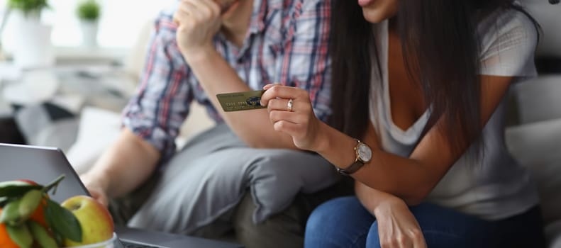 A married couple at home pays for purchases online, female hands with a credit card close-up. Ordering goods and products