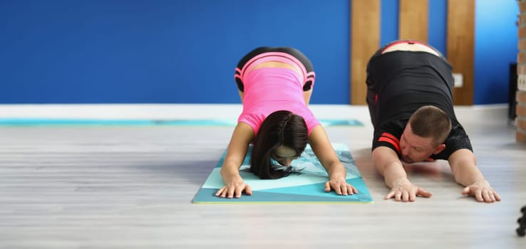 A man and a woman on the floor doing back stretches, close-up. Teaching sports exercises with a trainer in the gym