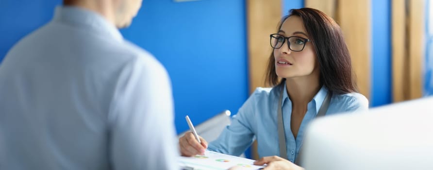 A woman in the office explains to a man a report with a diagram, close-up, blurry. Annual reporting, data analysis, correction