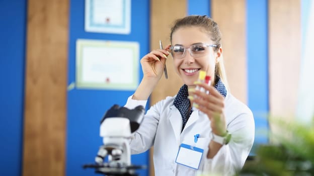 Beautiful woman laboratory assistant smiling holds a flask for blood tests, close-up, blurry. Clinic laboratory, microscope