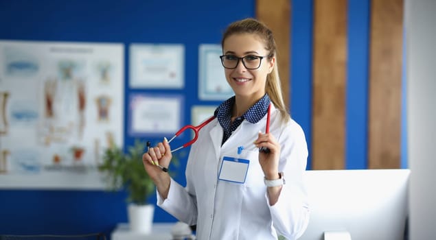 Young woman doctor smiling, standing in the clinic, close-up, blurry. Medical consultation, friendly hospital staff