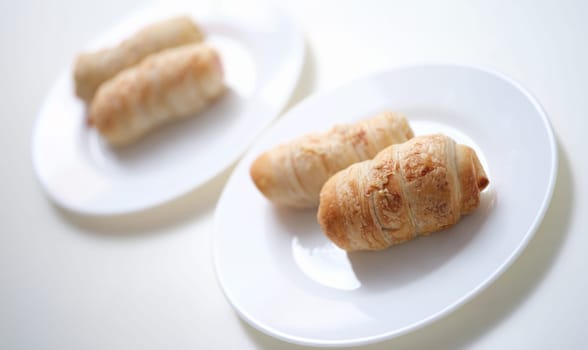 Puff crispy rolls on a white plate, sunny, close-up. Vegan baked goods. Quick breakfast, homemade dessert, pigs blanket