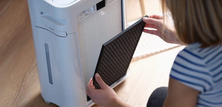 A woman is changing a replaceable filter of an air purifier, close-up. Household appliances for home, dust and odor removal