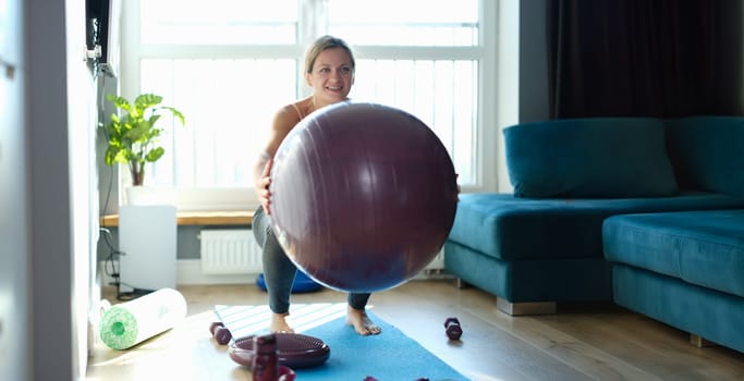 Woman doing squats with a ball at home, sunny, close-up. Fitball training. Strengthening the muscles of the abdomen and lower back