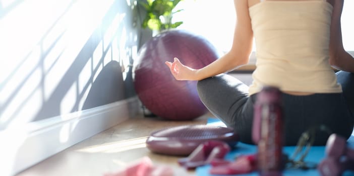 A woman after a workout sits on the floor in a yoga pose, view from the back, sunny. Meditation after sports activities, fitness at home