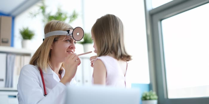 The pediatrician looks at the throat of a little girl, close-up. Visit to otolaryngologist, sick child. Family medicine