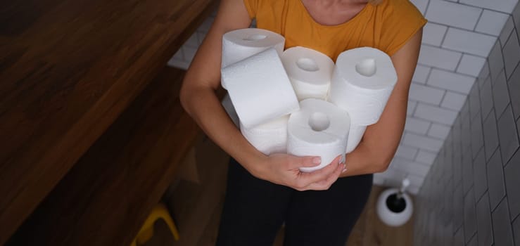 Woman in the toilet holds many rolls of toilet paper, close-up. Empty shelves, stock of personal care products