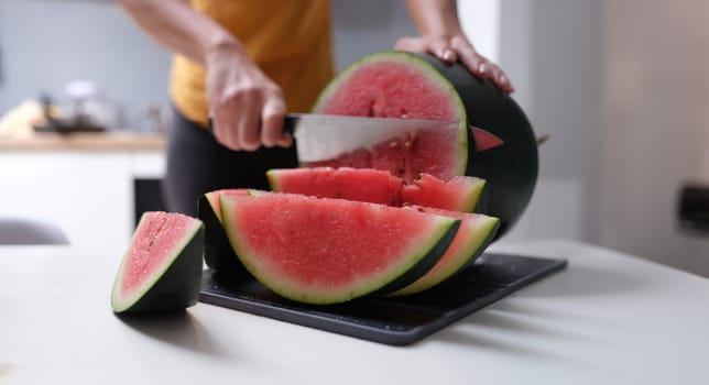 A woman in the kitchen cuts a watermelon, hands close-up, blurry. Juicy red fruit berry, vegetarian food