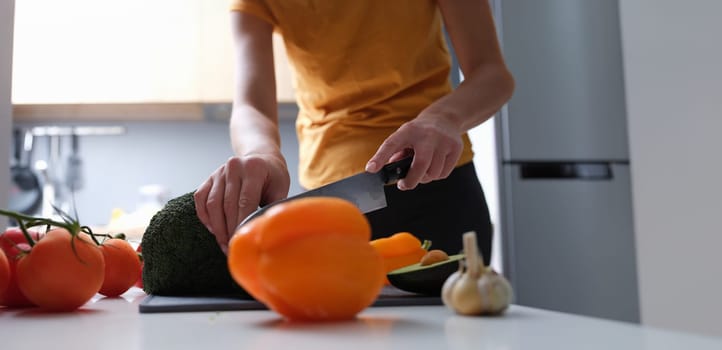 A woman in the kitchen is cutting vegetables, close-up. On the table broccoli, tomatoes, peppers, avocado and garlic