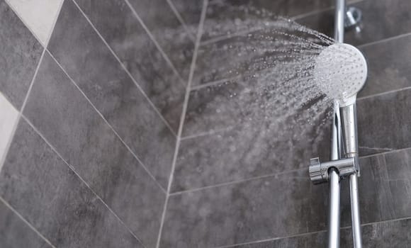 Water is pouring from the shower head into the shower room, close-up. Refreshing shower, cleanliness and hygiene