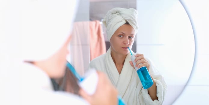 A woman in a dressing gown with a towel on her head is brushing her teeth with an irrigator. Oral hygiene, beauty and health