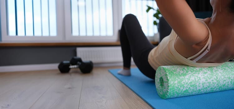 A woman lies on a sports roller, does exercises for the back at home, close-up. Fitness during quarantine