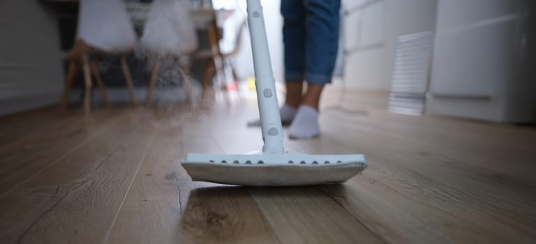 A steam mop washes the wooden parquet on the floor, close-up, blurry. Apartment cleaning, laminate flooring