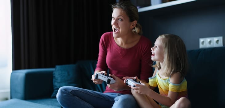 Little girl in the room with her mother playing video games, close-up. Gambling child's game, playstation