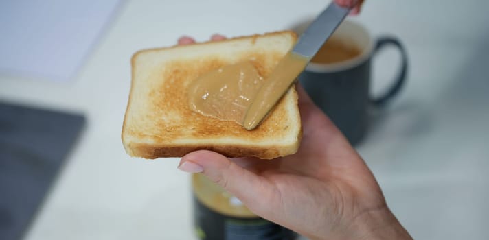 A hand smears peanut butter on a crispy toast made from bread. Traditional homemade American breakfast, unhealthy snack