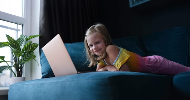 Happy little girl lies on the couch in front of a laptop, close-up. Child uses the Internet, cybersecurity