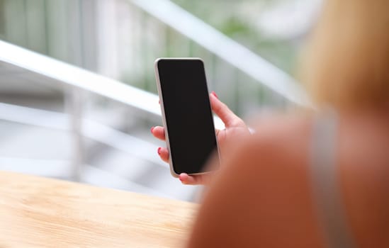 Woman holding a smartphone, sunny, hands close-up. The view from the back is blurry. Mobile phone black screen, mock up