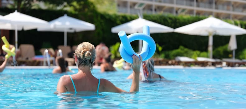 Woman in the pool doing exercises in the aquafitness group, back view, close-up. Relax on the water, wellness program