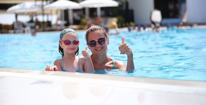 Mom and daughter in the pool show a thumbs up gesture, close-up. Goggles for sunbathing and swimming underwater, relaxation