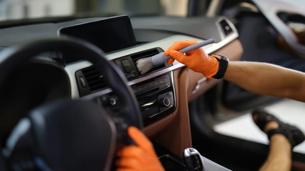 Male hands brush dust from the ventilation system in the car, close-up. Car interior, professional car cleaning service