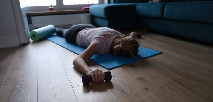 A woman exhausted by sports with dumbbells in her hands lies on the floor, close-up. Physical fatigue after fitness, muscle soreness