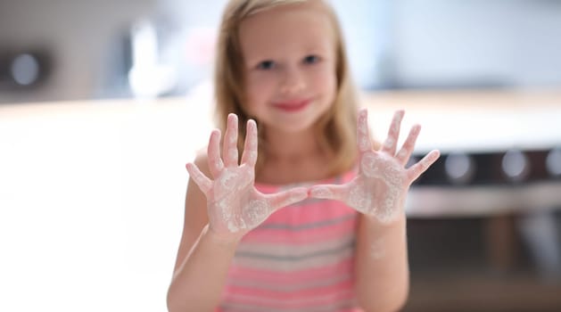 Little cute girl shows palms in flour, close-up, blurry. Teaching kids how to cook, online course on cooking at home