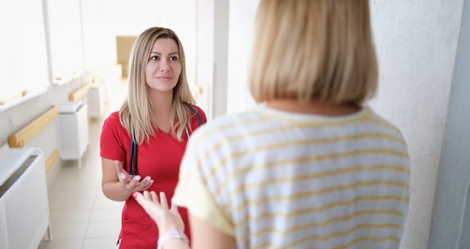 A doctor in a red uniform listens to a woman in the hospital corridor, close-up. Bloodless medicine, the position of the doctor