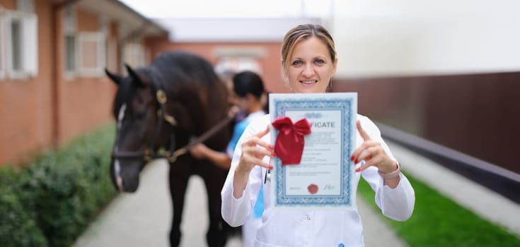 Happy woman vet doctor holding a horse certificate, close-up. Veterinary check-up in the stable. Equine Assisted Therapy