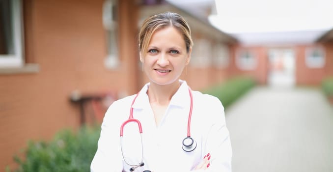 Doctor, a beautiful woman stands on the street against the background of the hospital, close-up, blurry. Ambulance service, clinic staff