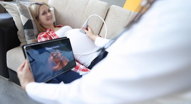 Doctor doing ultrasound of fetus to pregnant woman at home. Modern technologies in medicine concept