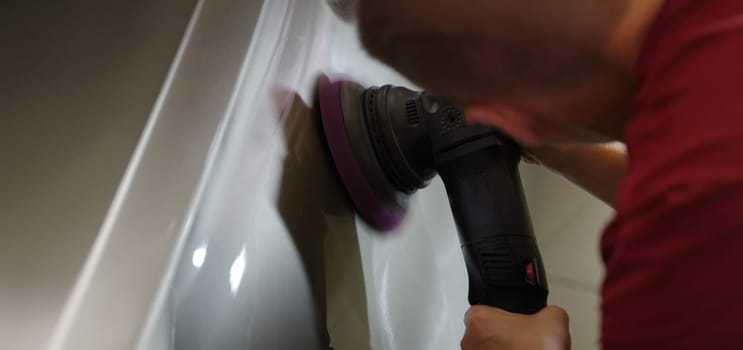 A man erases scratches on a car with a grinder, close-up. Automotive tools, car polishing equipment, detailing