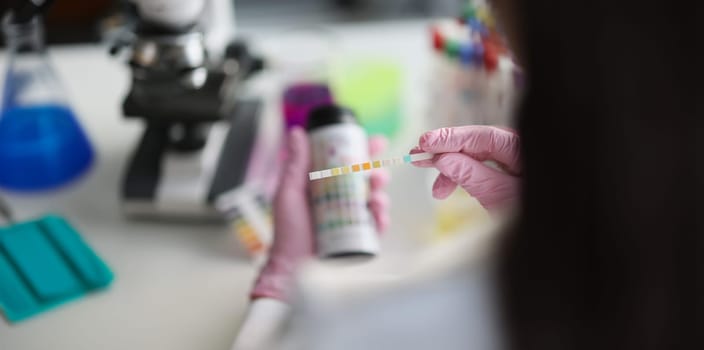 Gloved hands in the laboratory hold a litmus test strip, close-up, blurry. Bio samples for analysis. Ketones urine test
