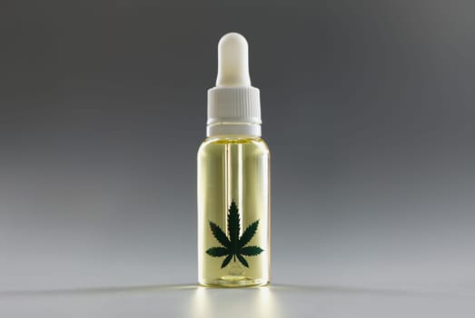 Hemp oil with a dispenser on a gray background, close-up. Pharmaceutical medical drug with cannabis, dropper