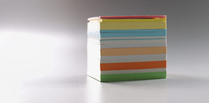 Multi-colored stack of paper for notes on a gray background, close-up. Different color blank post notes