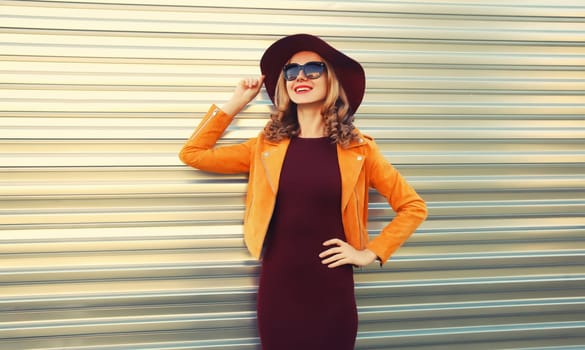 Beautiful smiling young woman wearing orange jacket, round hat on gray background