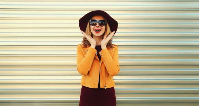 Happy excited surprised young woman wearing orange jacket, round hat on gray background
