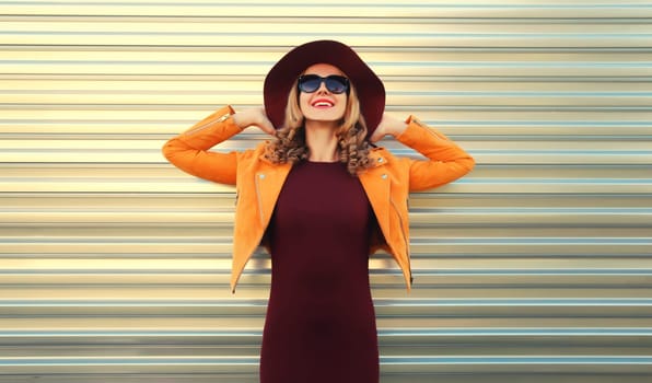 Beautiful happy smiling young woman wearing orange jacket, round hat on gray background