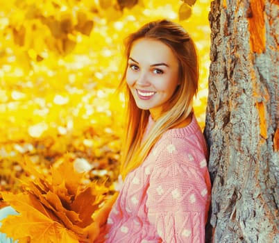 Portrait of beautiful happy smiling blonde woman with yellow maple leaves in autumn park