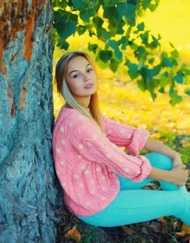 Beautiful young woman wearing pink sweater sitting in autumn park