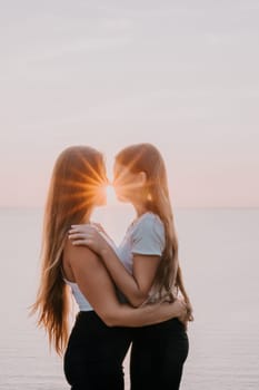 Two women stand close together, their faces nearly touching, with the setting sun creating a bright sunburst between them.